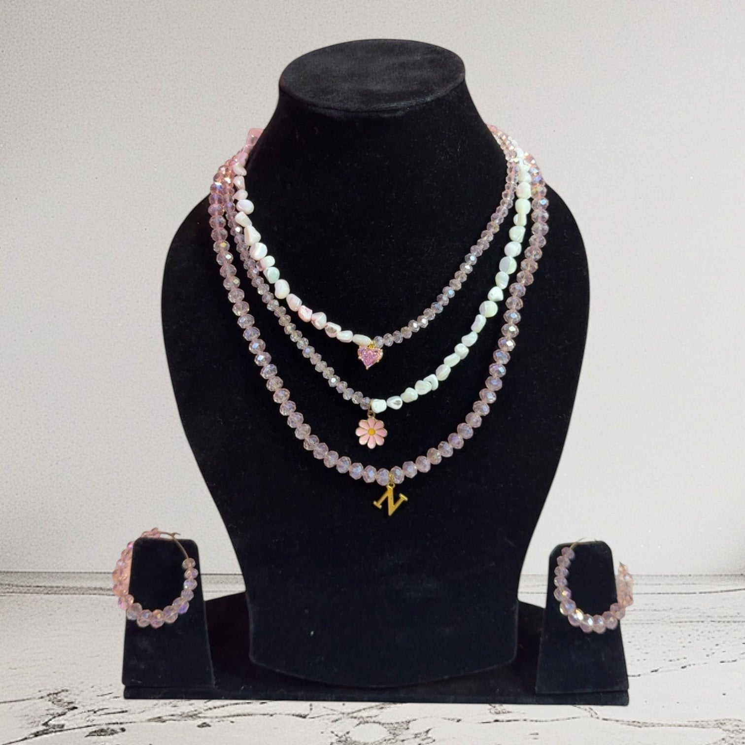Handmade Trinkets layered necklace with pink heart, flower, and N charm, paired with crystal bead hoop earrings. Pink and iridescent aurora finish.